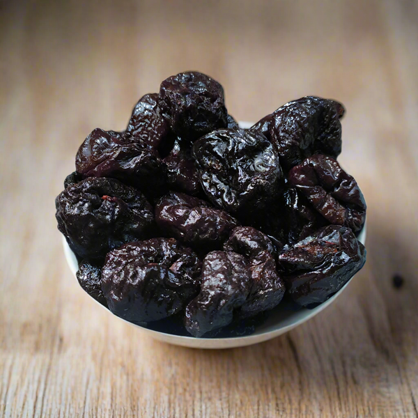 A bowl of dried prunes on a neutral background.
